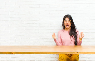young  pretty latin woman shouting aggressively with an angry expression or with fists clenched...