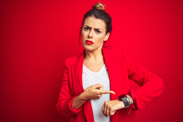 Young beautiful business woman standing over red isolated background In hurry pointing to watch time, impatience, upset and angry for deadline delay