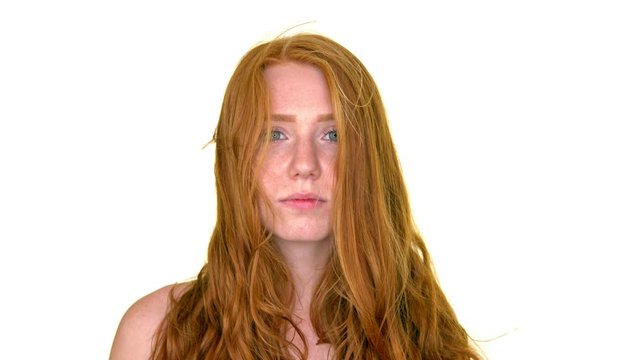 Portrait young redhead female looks at camera standing against white background slow motion