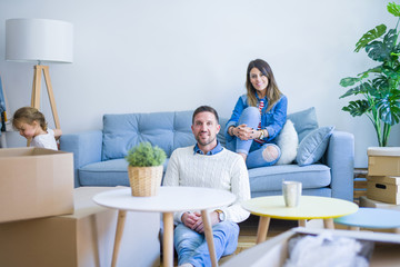 Beautiful family, parents sitting on the sofa drinking coffee looking his kid playing at new home around cardboard boxes