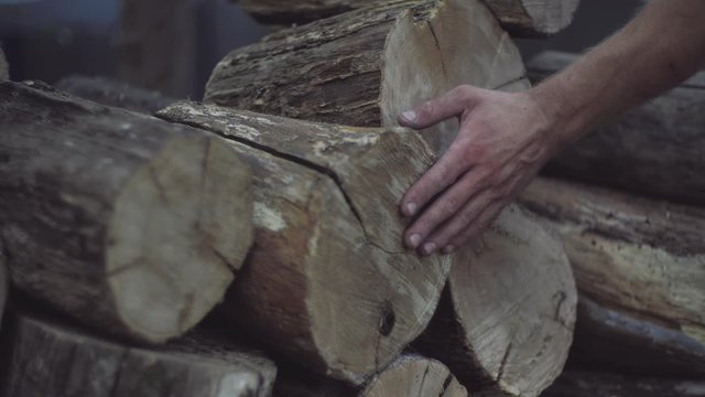 Man's hand touches the oak firewood blocks stored up for winter. Man's hand feels the wood structure of oak firewood blocks in a stack.