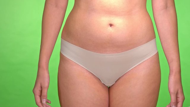 Woman covers her pelvis area ideal for feminine health care awareness  while light underwear panty on isolated green background