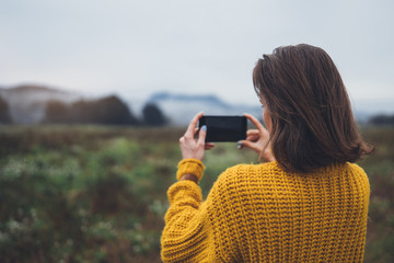 photographer girl hold in hands mobile phone taking photo on smartphone autumn foggy mountain, tourist shooting on photo camera on background landscape, internet online concept