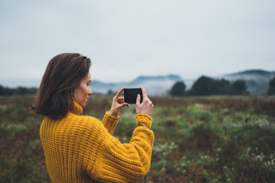 photographer girl hold in hands mobile phone taking photo on smartphone autumn foggy mountain, tourist shooting on photo camera, internet online concept