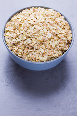 Dry oatmeal in bowl. Oat flakes on cement background. Cereals for making healthy breakfast. Vegetarian food. Copy space