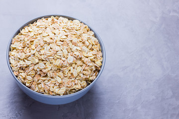 Dry oatmeal in bowl. Oat flakes on cement background. Cereals for making healthy breakfast. Vegetarian food. Copy space