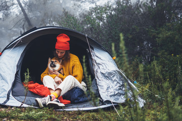 tourist traveler in camp tent hug red shiba inu on background foggy rain forest, woman with puppy...