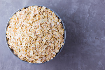 Dry oatmeal in bowl. Oat flakes on cement background. Cereals for making healthy breakfast. Vegetarian food. Copy space