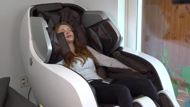 mid shot of beautiful young brunette European model enjoying a stylish black and white massage chair in a domestic setting. She appears relaxed and responsive to the vibration and massage part 5