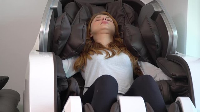 mid shot of beautiful young brunette European model enjoying a stylish black and white massage chair in a domestic setting. She appears relaxed and responsive to the vibration and massage part 8