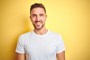 Obraz premium Young handsome man wearing casual white t-shirt over yellow isolated background with a happy and cool smile on face. Lucky person.