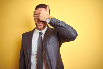 Young handsome business man over yellow isolated background smiling and laughing with hand on face covering eyes for surprise. Blind concept.