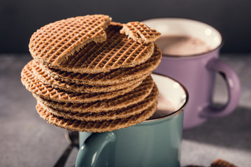 Traditional dutch cookies syrupwaffles over old mug with chocolate milk on gray background with copy space. Retro style toned.