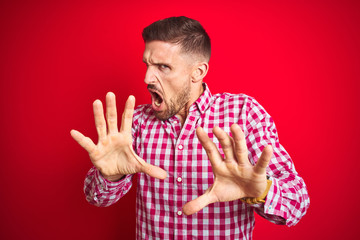 Naklejka premium Young handsome man over red isolated background afraid and terrified with fear expression stop gesture with hands, shouting in shock. Panic concept.