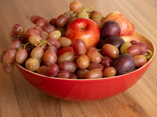 mixed set of fresh raw ripe fruits apple plums and grape on wooden plate isolated on the wooden background