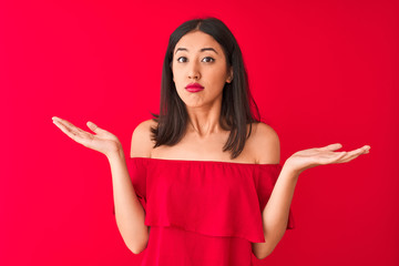 Young beautiful chinese woman wearing casual t-shirt standing over isolated red background clueless...