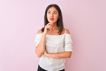 Beautiful chinese woman wearing white t-shirt standing over isolated pink background with hand on chin thinking about question, pensive expression. Smiling with thoughtful face. Doubt concept.