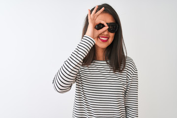 Chinese woman wearing striped t-shirt and sunglasses standing over isolated white background doing ok gesture with hand smiling, eye looking through fingers with happy face.