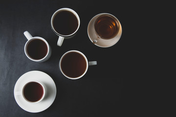 Top view of many cups, mugs with hot tea drink on dark background, copy space. Tea time or tea brake. Autumn toned, dark photo.