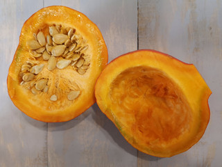 A pumpkin, cut in half, lies on a wooden surface. One half of the pumpkin with seeds, the other is cleared of seeds.