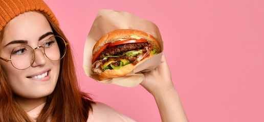 Beautiful teenage girl with red hair and hat holding burger and beverage in both hands. Ginger...