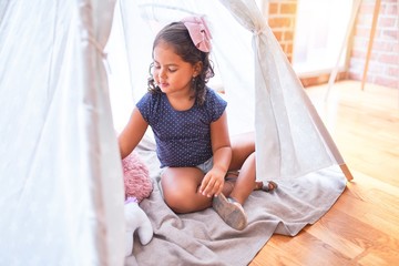 Beautiful toddler girl sitting on the floor playing with unicorn and doll inside  tipi at...