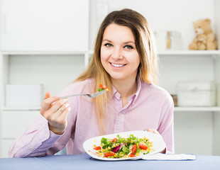 Obraz na płótnie Canvas Young positive woman trying tasty green salad