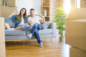 Young beautiful couple relaxing sitting on the sofa around boxes from moving to new house looking confident with smile on face, pointing oneself with fingers proud and happy.