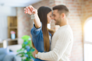 Young couple moving to a new home, hugging in love showing keys of new apartment smiling very happy