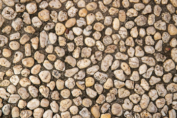 Grungy photo texture of pebble paving, top view background. White pebbles in grey sand top view.