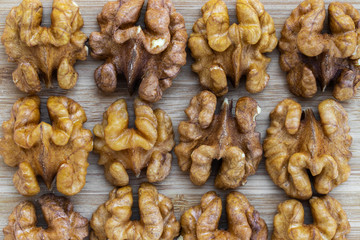 Unshelled walnuts are laid out in rows on a brown wooden surface