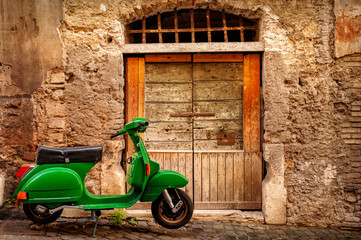 Fototapeta premium Green scooter near an old wall in Rome, Italy. Exterior, architecture and landmark of ancient streets in Rome.