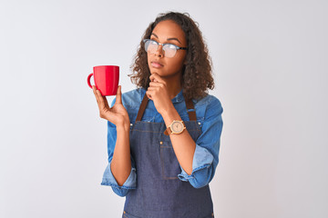 Brazilian barista woman wearing apron drinking cup of coffee over isolated white background serious face thinking about question, very confused idea