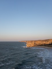 Crimean seascape with small waves, clear blue sky and distant rocks at sunset copy space