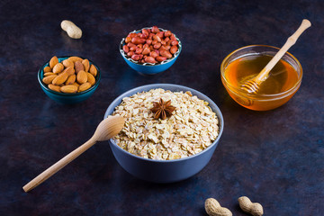 Dry oatmeal, nuts and honey. Oatmeal and almond nuts on dark background. Cereal and peanuts for making healthy breakfast. Vegetarian food