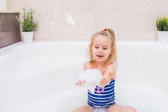 Little blonde girl taking bubble bath in beautiful bathroom.Kids hygiene. Shampoo, hair treatment and soap for children. Kid bathing in large tub.
