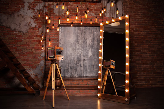 a very old rarity photo camera stands on a tripod near a huge mirror with lights in the Studio with brick background. nobody. copy space.