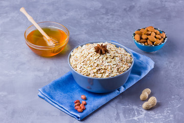 Dry oatmeal, nuts and honey. Oatmeal and almond nuts on cement background. Cereal and peanuts for making healthy breakfast. Oatmeal in bowl on blue napkin