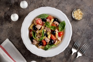 Salad with canned tuna, pasta, cherry tomatoes, olives, parmesan, olive oil and basil. Top view. 
