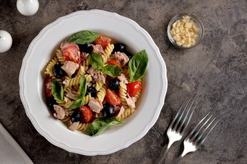 Salad with canned tuna, pasta, cherry tomatoes, olives, parmesan, olive oil and basil. Top view. 