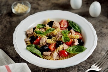 Salad with canned tuna, pasta, cherry tomatoes, olives, parmesan, olive oil and basil. Top view. 