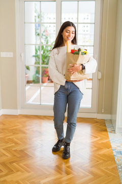 Beautiful young woman smiling holding a paper bag full of fresh groceries at home