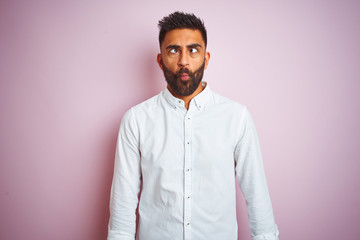 Young indian businessman wearing elegant shirt standing over isolated pink background making fish face with lips, crazy and comical gesture. Funny expression.