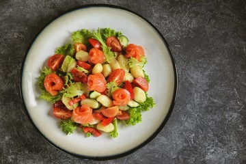 Healthy potato gnocchi salad with cherry tomatoes, cucumber, bell pepper, slightly salted salmon, olive oil and lettuce. Top view. 