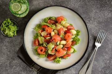 Healthy potato gnocchi salad with cherry tomatoes, cucumber, bell pepper, slightly salted salmon, olive oil and lettuce. Top view. 