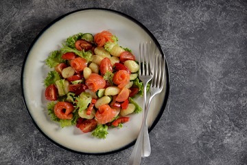 Healthy potato gnocchi salad with cherry tomatoes, cucumber, bell pepper, slightly salted salmon, olive oil and lettuce. Top view. 