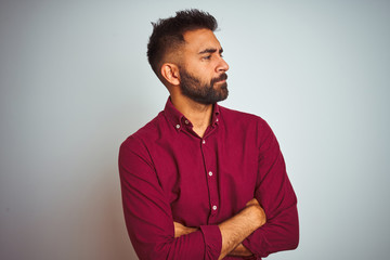 Young indian man wearing red elegant shirt standing over isolated grey background looking to the side with arms crossed convinced and confident