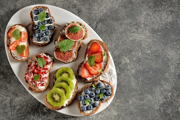 Healthy vegetarian sandwiches made from rye bread with soft cheese, organic berries and fruits - strawberries, blueberries, kiwi, figs, pomegranate seeds and mint.