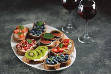 Healthy vegetarian sandwiches made from rye bread with soft cheese, organic berries and fruits - strawberries, blueberries, kiwi, figs, pomegranate seeds and mint.