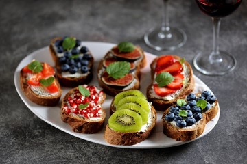 Healthy vegetarian sandwiches made from rye bread with soft cheese, organic berries and fruits - strawberries, blueberries, kiwi, figs, pomegranate seeds and mint.